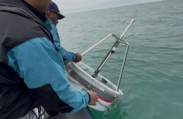 Two people on a small boat lowering the unballasted buoy into the sea off Brighton.