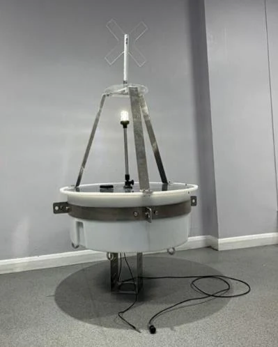 The completed buoy prototype standing on its base: a free-flooded HDPE shell with a bolted aluminium tripod, mast, daymark cross and navigation light.